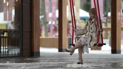 Romantic Lady Is Resting Alone in Amusement Park at Winter Day Swinging on Swing Smiling