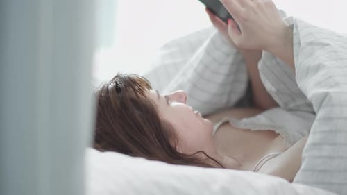 Woman Uses Phone Lying Down in Bed