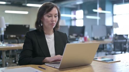 Ernsthafte Geschäftsfrau mittleren Alters arbeitet im Büro am Laptop