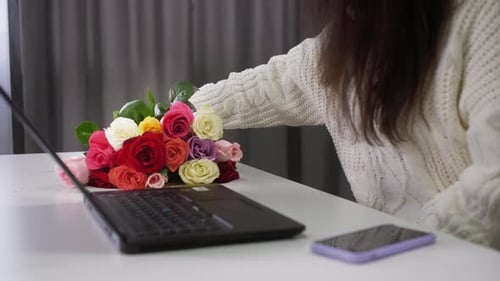 Closeup View of Woman Holding Flower Bouquet and Typing on Laptop