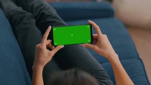 Freelancer Sitting on Sofa While Looking at Movies Using Phone in Horizontal Mode with Mock Up Green