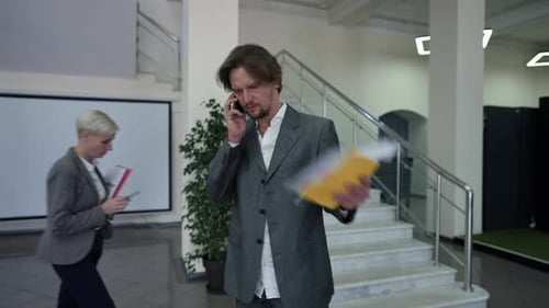 Stressed Troubled Caucasian Man Talking on Phone Shaking Paperwork Walking in Office Lobby with