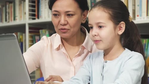 Girl Learns on Laptop with Woman in Library