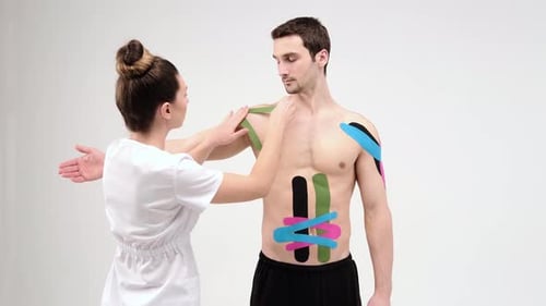 El médico pega una cinta de tratamiento especial a la malla del hombro. El fisioterapeuta pega cintas de kinesio