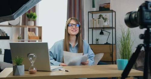Chica con auriculares inalámbricos sentada frente a la cámara durante una videollamada en línea con espectadores