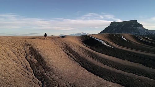 Lone person walking on ridge in desert through eroded landscape