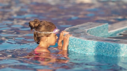 A Girl in a Bright Swimsuit with Swimming Goggles Dives Into a Pool with Clear Transparent Water