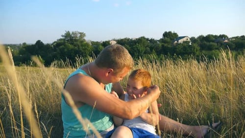 Joyeux jeune homme allongé sur l'herbe au champ et jouant avec son petit garçon