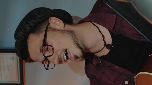 Close Up of Bearded Guy in Hat Emotionally Singing Into Microphone and Playing Guitar in Home Studio