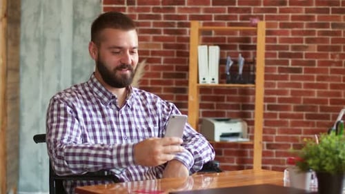 Man in Wheelchair Using Smartphone at Desk Indoors