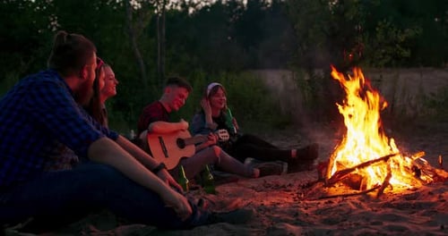 Friends Gathered Around Campfire Playing Guitar at Night