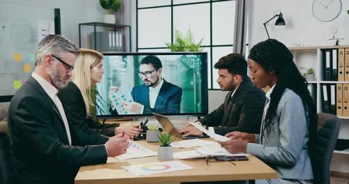 Los empresarios tienen una videoconferencia con su colega masculino en la televisión durante la reunión