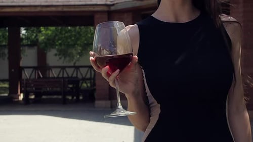 Mujer elegante con una copa de vino caminando en el jardín de la mansión