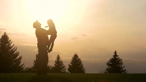 Padre levantando a su hija en el parque mientras se pone el sol.