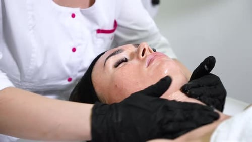 Mains d'esthéticienne appliquant une lotion et massant le visage de la femme