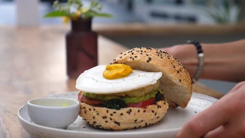 Hand Serving Vegan Burger with Plant Based Egg on Top
