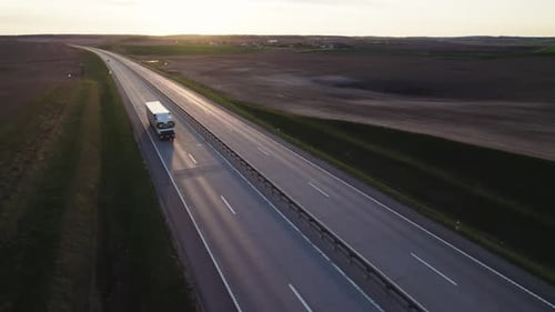 Large truck with cargo trailer is driving along the highway at high speed at sunset.