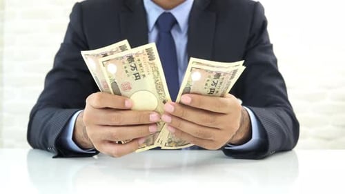 Businessman counting money, Japanese yen banknotes, at the table