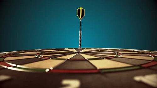 Darts arrow hitting in the bullseye of the dartboard hanging on the dark wall.