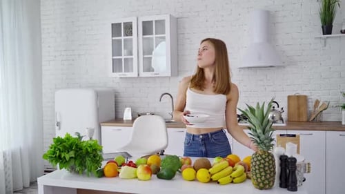 Woman Eating Berries in Bright Kitchen with Fruit