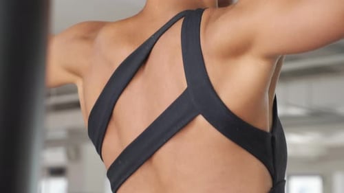 Muscles on the Back of a Woman Pulling Up on the Bar in Gym