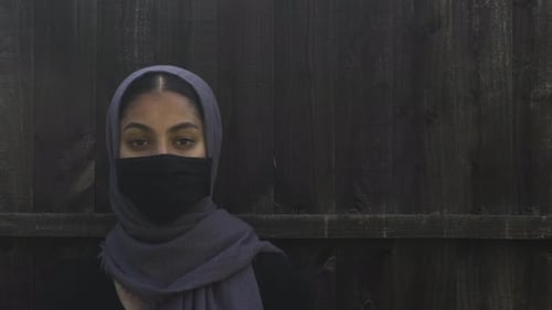 Female Teenager Wearing Headscarf And Face Mask Outside Against Fence. Locked Off