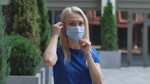 Woman Puts on Surgical Mask Outside Building
