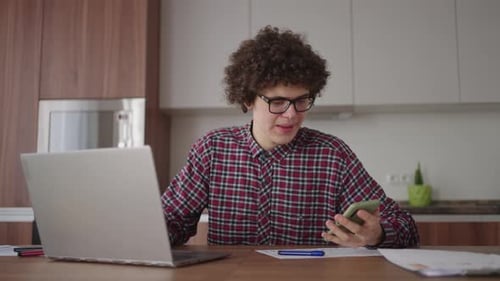 Young Adult Working From Home Using Laptop and Phone