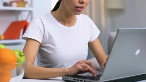 Woman Eating Apple and Using Laptop at Home