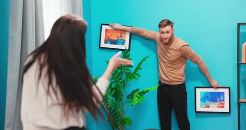 Couple Decorating Home, Hanging Pictures on Teal Wall