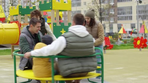 Glückliche Nachbarn unterhalten Kinder beim Karussell auf dem Spielplatz