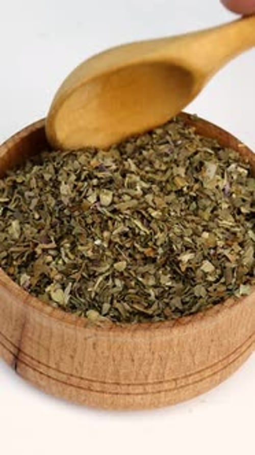 Dried Basil in Wooden Bowl Being Scooped