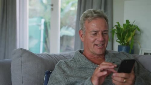 Mature Man Relaxing on Couch Using Smartphone