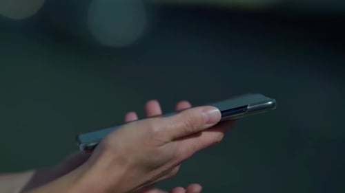 Side View. Hands of a Woman Using a Smartphone in the Street, Typing a Message. Close - Up of a