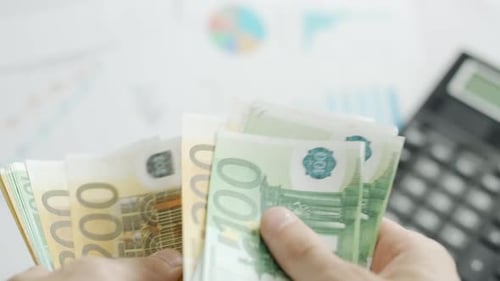A Businessman Hands are Counting Euro Bill Notes on Background of Calculator and Graphs