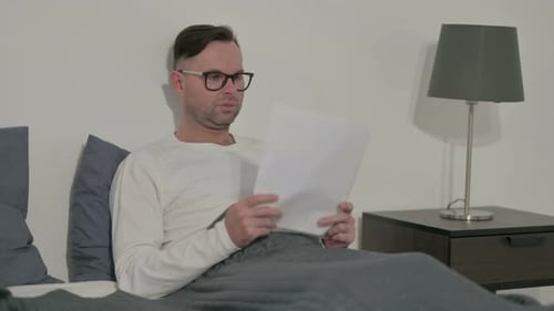 Man Reads Documents in Bed at Home