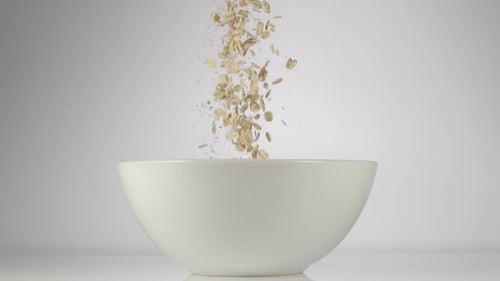 Oats Being Poured Into a White Bowl
