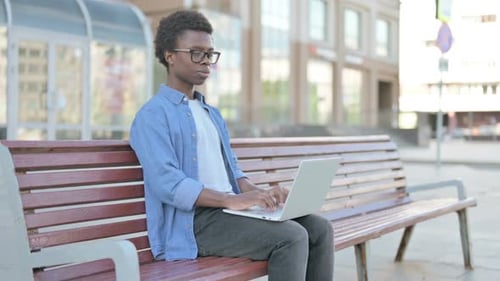 Young Man Smiling, Using Laptop on Bench