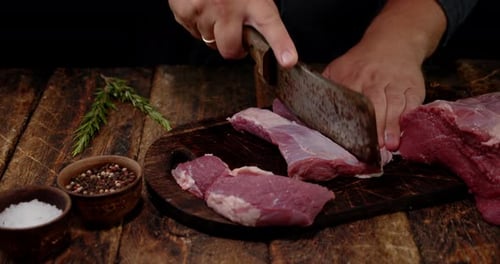 Hands Cutting Raw Meat on Wooden Board