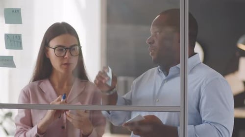 Team Brainstorming Ideas on Glass Wall in Office