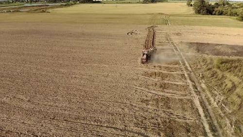 Tracteur puissant équipé d'une charrue cultivant le champ et soulevant d'énormes nuages de poussière brune suffocante