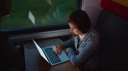 Woman Working on Laptop While Riding Train at Night