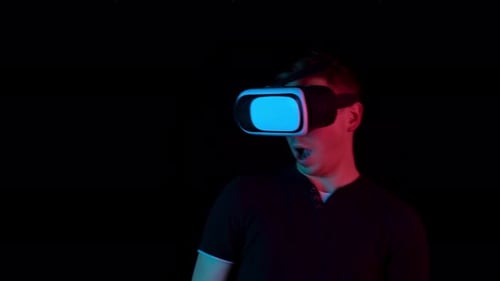 Jeune homme aux lunettes VR. Un homme immergé dans la réalité virtuelle fait des mouvements avec ses mains. Bleu et