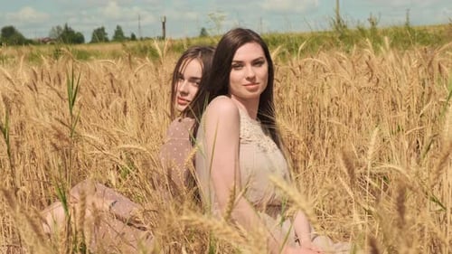 Two Enchanting LGBT Women Sitting in Wheat Field in Beautiful Dresses and Looking at Each Other