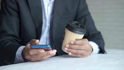 Business Man Hand Using Smart Phone and Paper Coffee Cup on Table