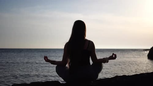 Jeune femme aux cheveux longs pratiquant des étirements en plein air sur un tapis de yoga au bord de la mer sur un coucher de soleil chaud