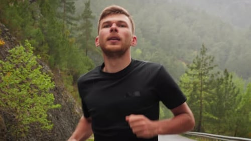 Man Runs on a Road Through Forest in Rain