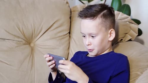 Excited Boy Using Smartphone on Comfortable Couch