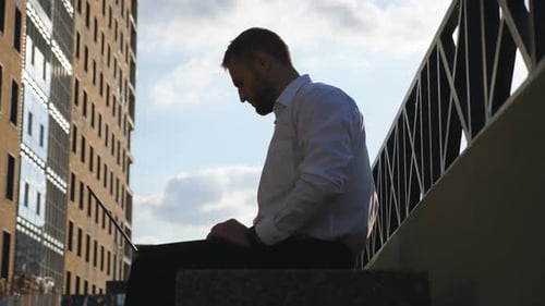 Young Businessman Works on Notebook Sitting on Bench at City