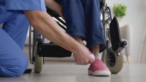 Medical Professional Assists Person in Wheelchair With Footrests